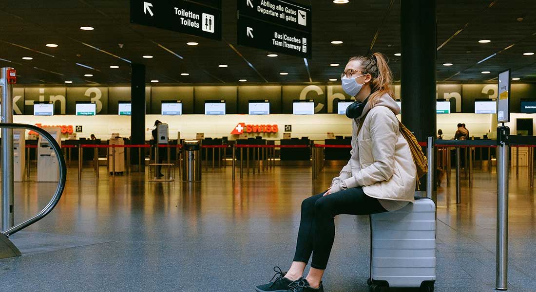 Kvinde med mundbind siddende på kuffert i lufthavn