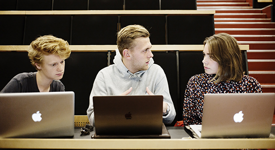 Tre unge studerende med computere i undervisningslokale